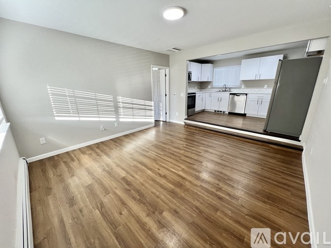 A spacious room with wooden flooring and a kitchen area in the background.