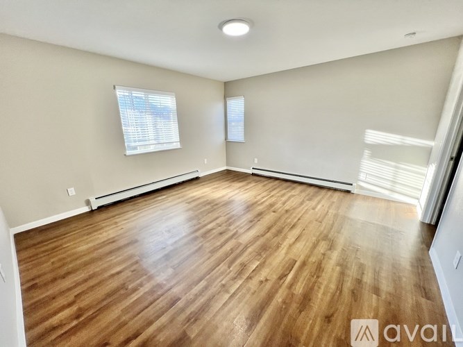 A room with wooden flooring and two windows.