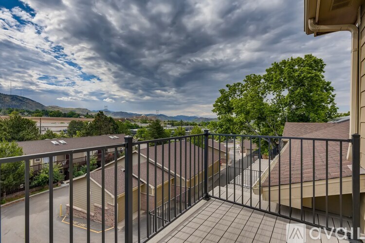 A balcony with a metal railing overlooks a parking lot and distant hills.