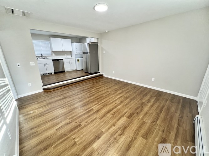 A spacious room with wooden flooring and a kitchen area in the background.