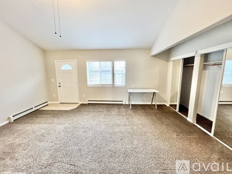 A room with a carpeted floor, a white door, a table, and a window.