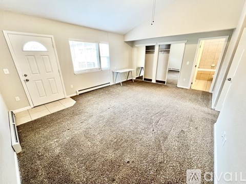 A spacious room with a carpeted floor and a door on the left side.