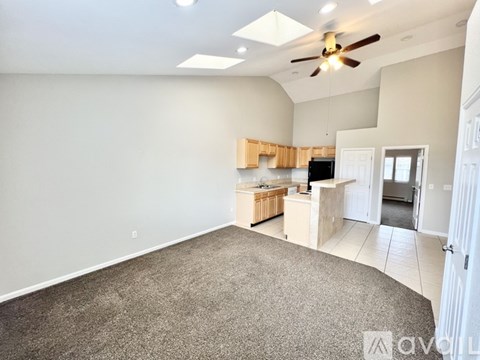 A spacious living room with a ceiling fan and a kitchen area in the background.