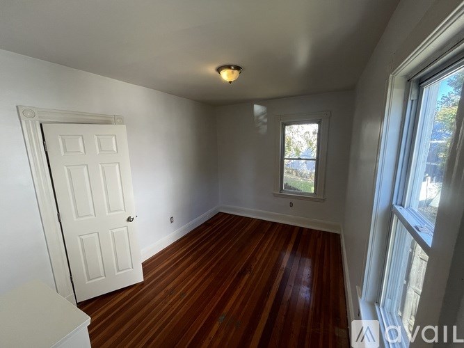 A room with a white door and a window with a view of trees outside.
