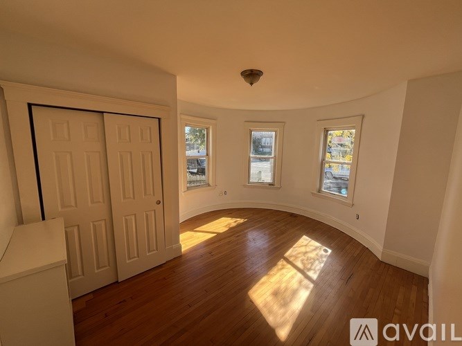 A room with wooden floors and white walls, with a door on the left and two windows on the right.
