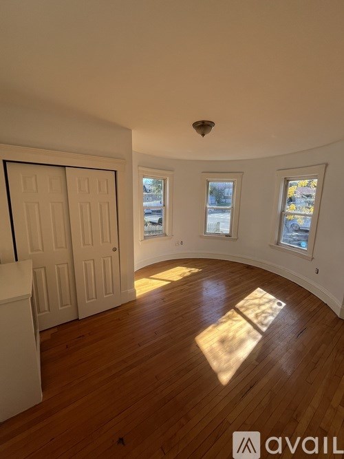 A room with wooden floors and white walls, featuring a white door and two windows with stained glass.