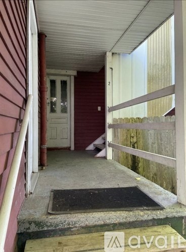 A red house with a white door and a black mat on the porch.