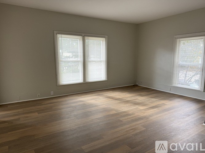 A room with wooden flooring and two windows.