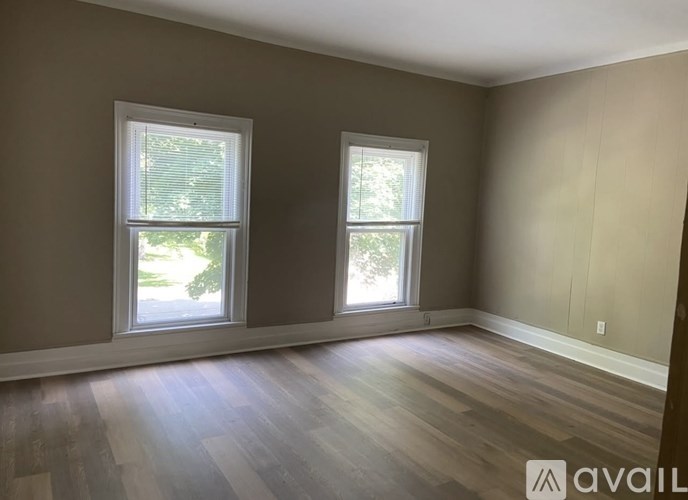 A room with two windows and wooden flooring is available for rent.
