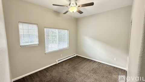 A room with a carpeted floor, a ceiling fan, and two windows with blinds.