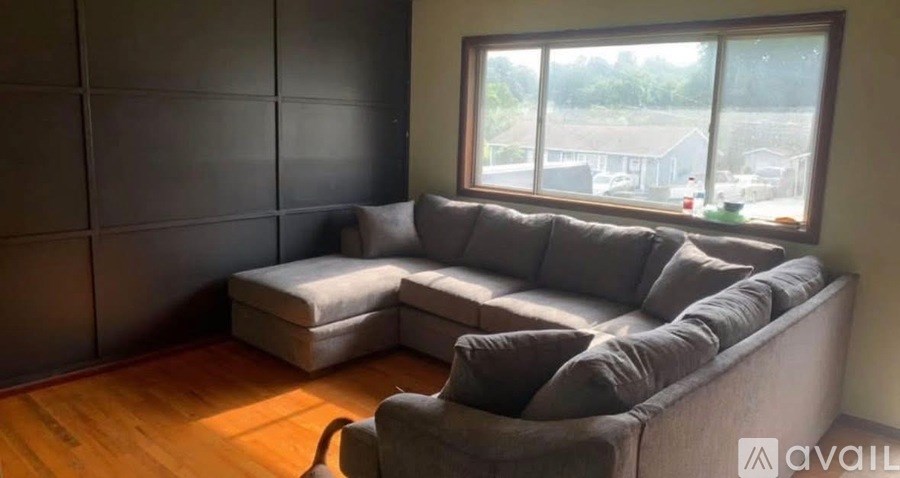A grey couch with a white pillow is in front of a window.