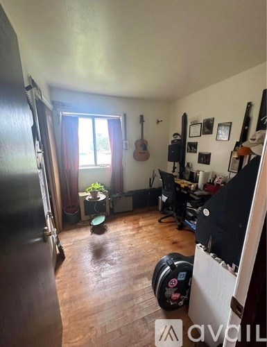 A room with a guitar hanging on the wall and a black barrel-shaped speaker.