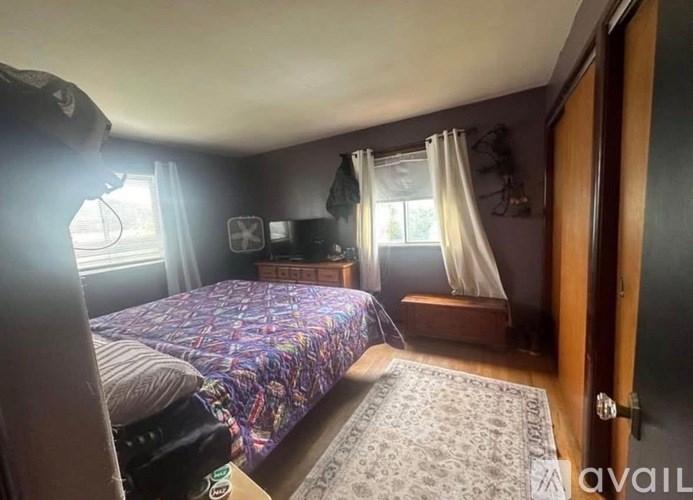 A bedroom with a bed, a window with curtains, and a rug on the floor.