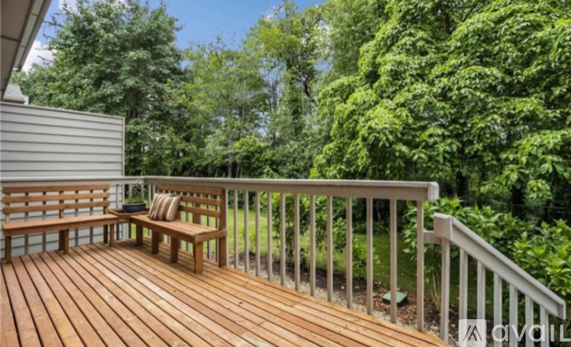A wooden deck with a bench and a pillow is surrounded by greenery.