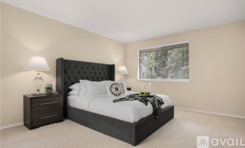 A bedroom with a large bed, a nightstand with a lamp, and a window with a view of trees.