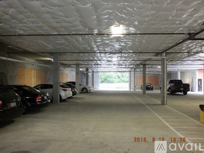 A parking garage with cars parked on the left side and a yellow trash can on the right side.