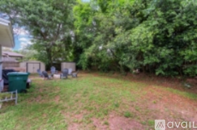A backyard with a green trash can and a tree.