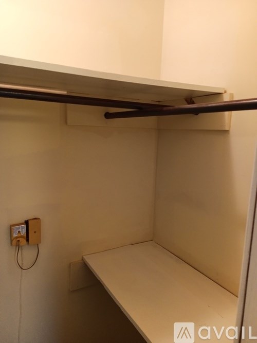 A small, empty room with a shelf and a wall-mounted electrical outlet.