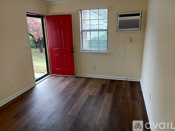 A room with a red door, a window with blinds, and a wall-mounted air conditioner unit.