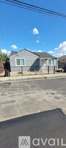 A grey house with a black fence and a blue sky in the background.