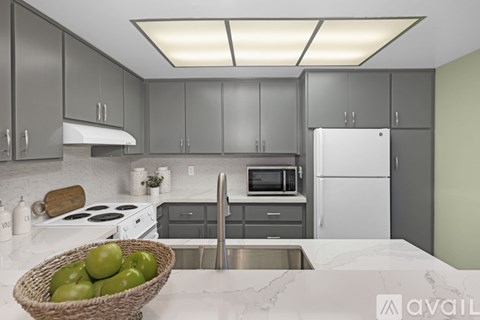 A kitchen with a white counter top and a basket of green apples on it.