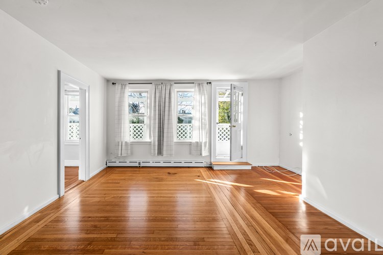 A room with wooden floors and white walls, with a view of the outside through the windows.