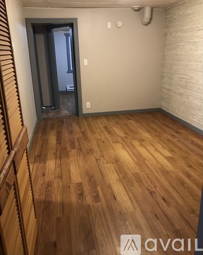 A room with wooden flooring and a door leading to another room.