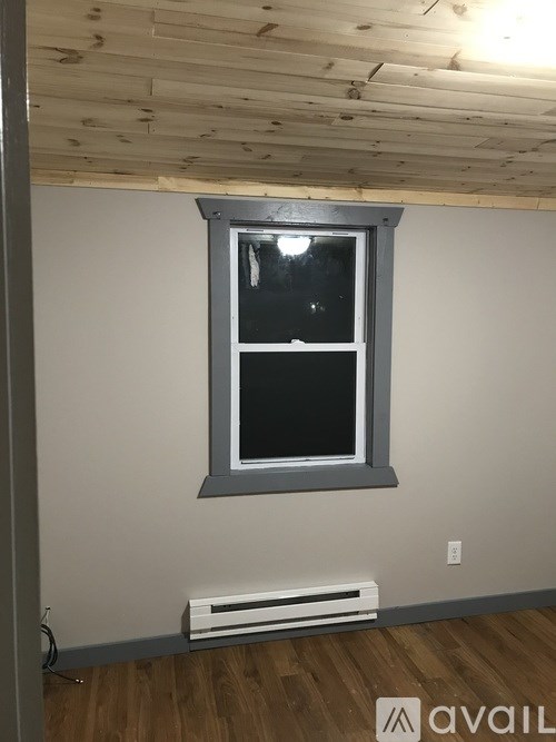 A window with a white frame and black window pane is on a white wall.
