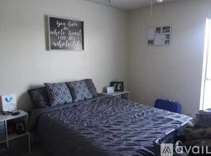 A bedroom with a bed, pillows, a nightstand, and a framed sign on the wall.