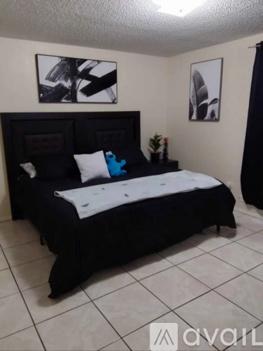 A black bed with white pillows and a white blanket in a room with two pictures on the wall.