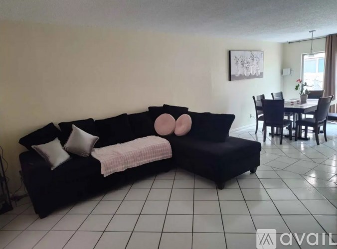A black couch with a pink pillow and a white pillow on it in a room with a dining table and chairs.