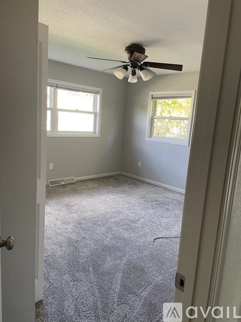 A room with a ceiling fan and two windows.
