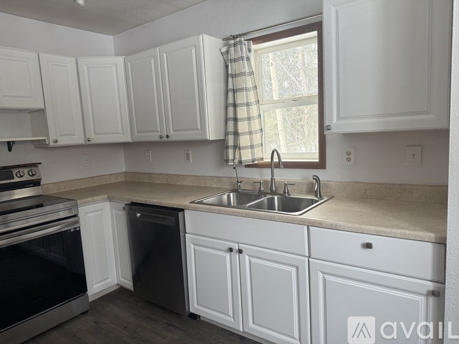 A kitchen with white cabinets and a window with a checkered curtain.
