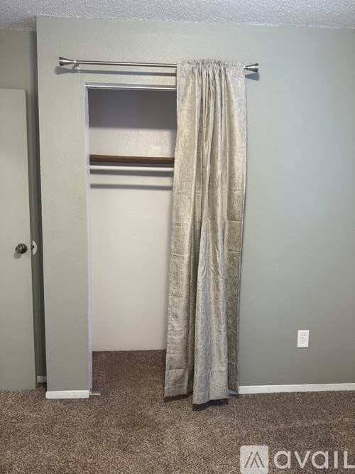 A room with a carpeted floor, a grey door, and a curtain.