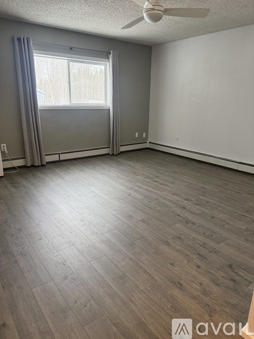 A room with wooden flooring and a window with curtains.