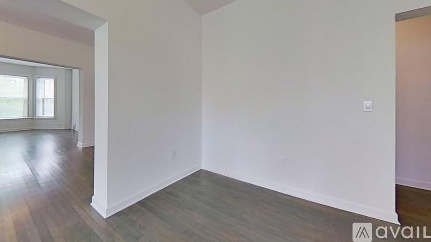 A room with wooden floors and white walls, with a window on the left side.