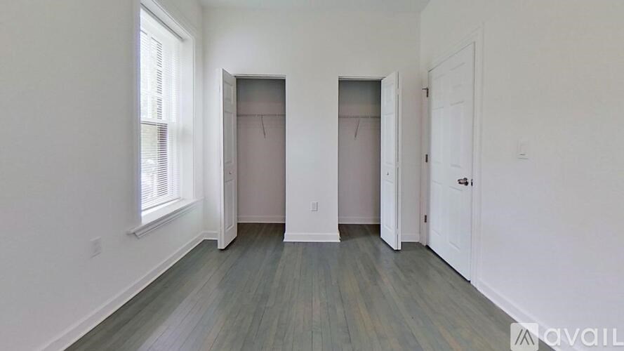 A room with a grey floor and white walls, with a window on the left and two doors on the right.