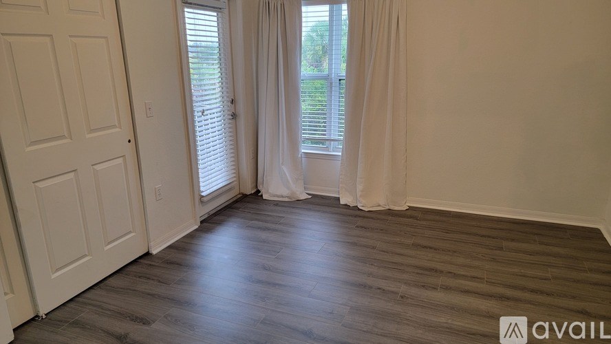 A room with a wooden floor and a window with white curtains.