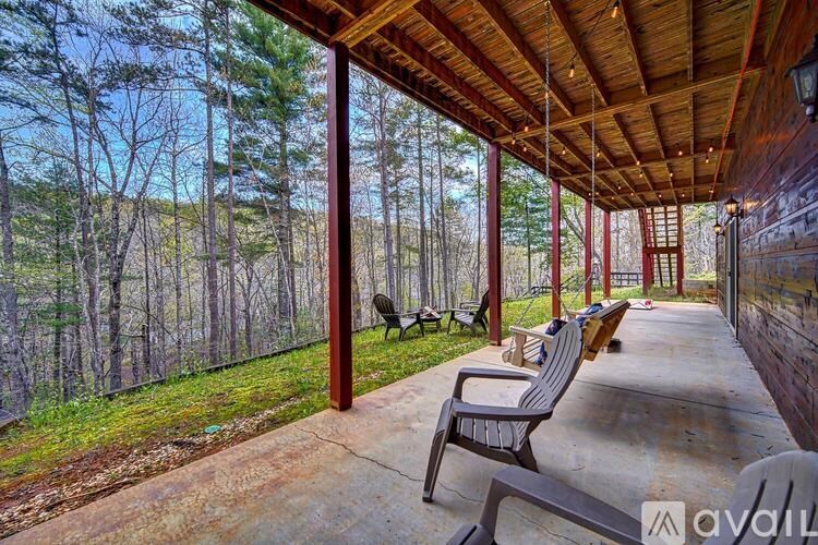 A porch with a wooden ceiling and benches overlooks a wooded area.