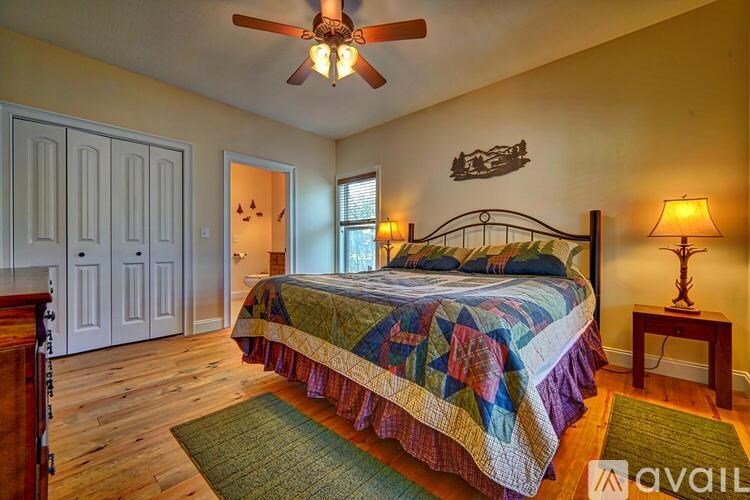 A bedroom with a bed, a ceiling fan, and a wooden floor.