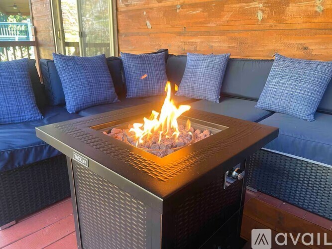 A modern fire pit is in the middle of a patio with a blue couch and pillows.
