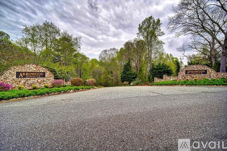 The image shows a road leading to a sign that reads "Arrowood" with a backdrop of trees and a cloudy sky.