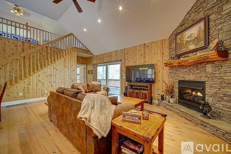 A living room with a stone fireplace and a wooden staircase.