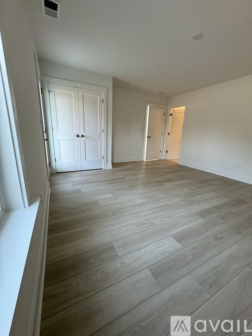 A spacious room with wooden flooring and white walls.