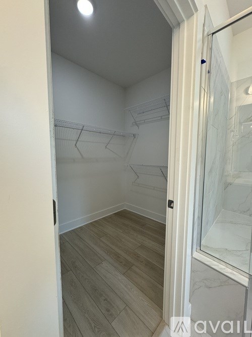 A white door with a glass window is open to a room with wooden flooring and white walls.