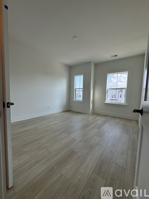A room with wooden flooring and two windows.