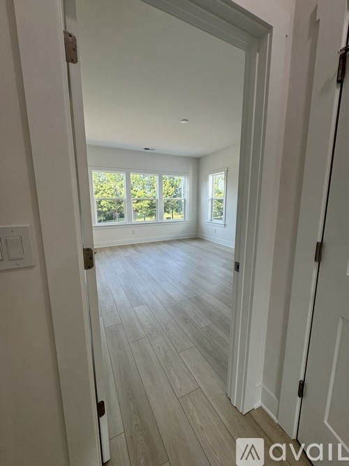 A room with white walls and wooden flooring, with a doorway leading to another room.