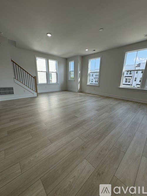 A spacious room with wooden flooring and large windows.