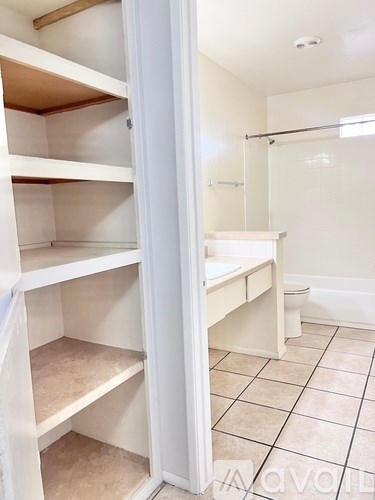 A white closet with shelves and a toilet in the background.