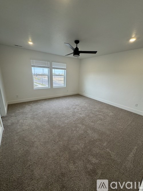 A room with a carpeted floor, a ceiling fan, and a window with blinds.